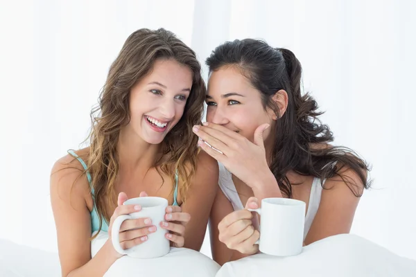 Female friends with coffee cups gossiping in bed — Stock Photo, Image