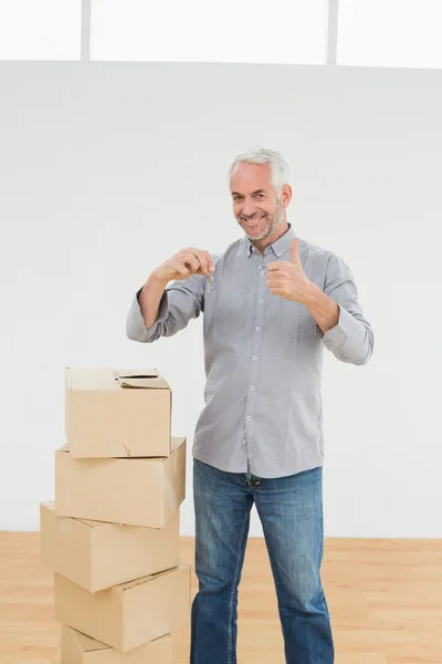 Hombre con cajas y llaves señalando pulgares en una casa nueva — Foto de Stock