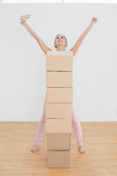 Mujer con cajas y pincel levantando manos en casa nueva — Foto de Stock