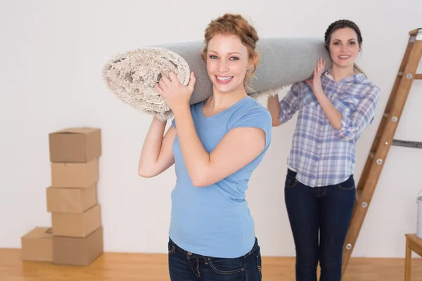 Amici sorridenti che trasportano tappeto arrotolato dopo essersi trasferiti in una casa — Foto Stock