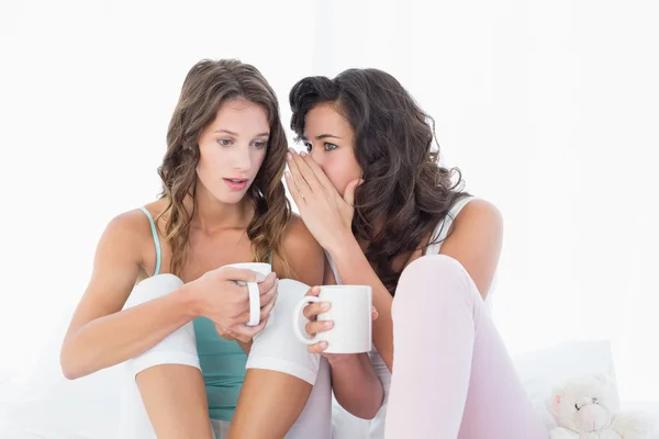 Ontspannen vriendinnen met koffie cups roddelen in bed — Stockfoto