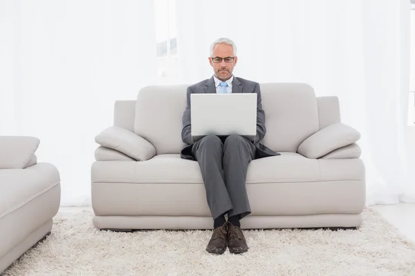 Concentrated businessman using laptop on sofa in living room — Stock Photo, Image