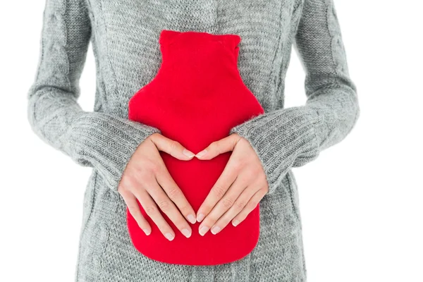 Seção média de uma mulher segurando saco de água quente vermelho no abdômen — Fotografia de Stock