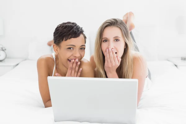 Geschokt jonge vrouwelijke vrienden met laptop in bed — Stockfoto
