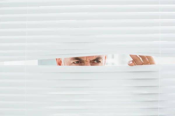 Ernstige volwassen zakenman gluren door blinds — Stockfoto