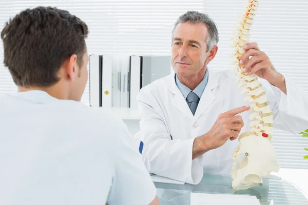 Médico explicando la columna vertebral a un paciente en el consultorio — Foto de Stock