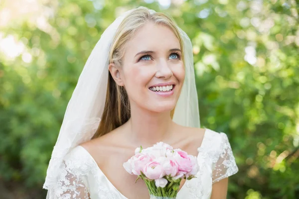 Jolie mariée souriante tenant son bouquet portant un voile levant les yeux — Photo