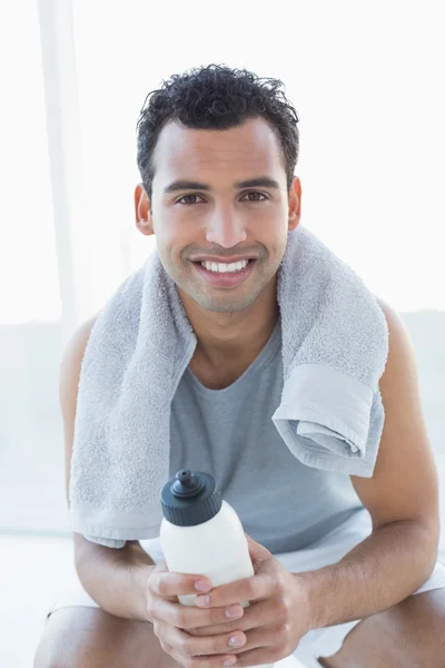 Man with towel around neck holding water bottle in fitness studio — Stock Photo, Image