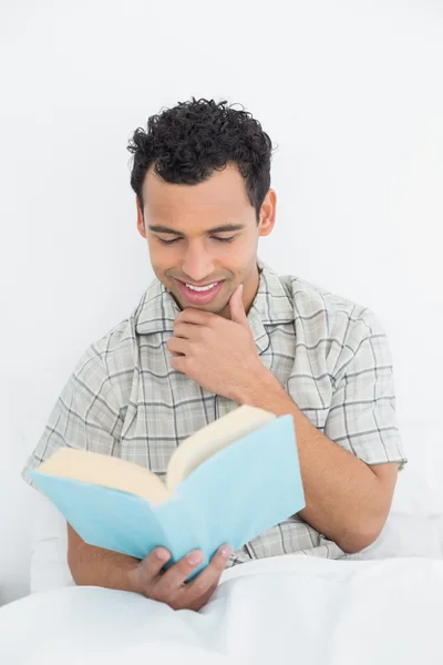 Lächelnder junger Mann liest Buch im Bett — Stockfoto