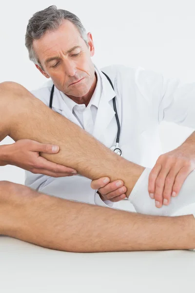Побочный обзор зрелого врача, осматривающего колено пациента — стоковое фото