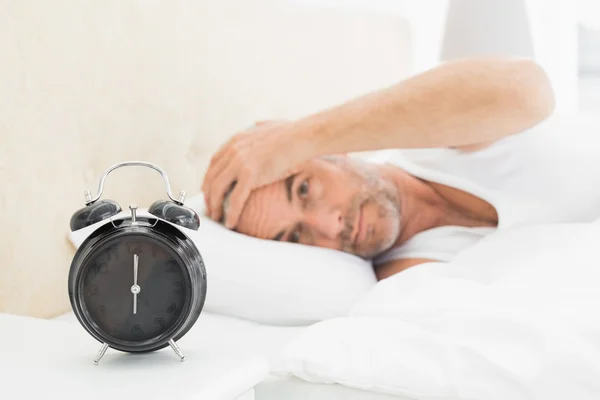 Hombre descansando en la cama con despertador en primer plano —  Fotos de Stock