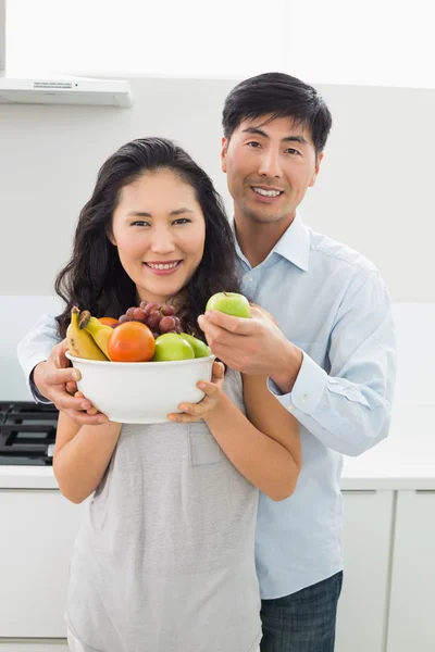 Jovem casal segurando tigela cheia de frutas na cozinha — Fotografia de Stock