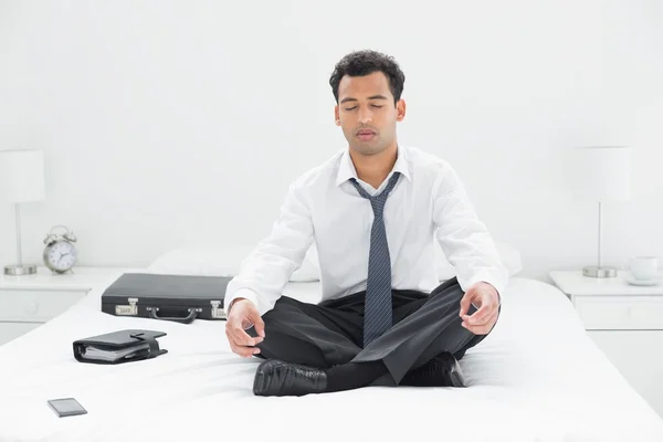 Relaxed young businessman sitting in lotus pose on bed — Stock Photo, Image