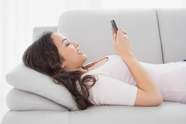 Jonge vrouw voor SMS-berichten op sofa thuis glimlachen — Stockfoto