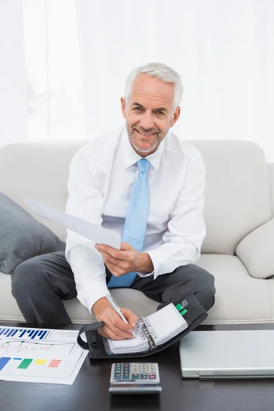 Lächelnder Geschäftsmann mit Grafiken und Tagebuch zu Hause — Stockfoto