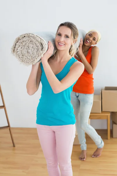 Kvindelige venner transporterer rullet tæppe efter at have flyttet i et hus - Stock-foto