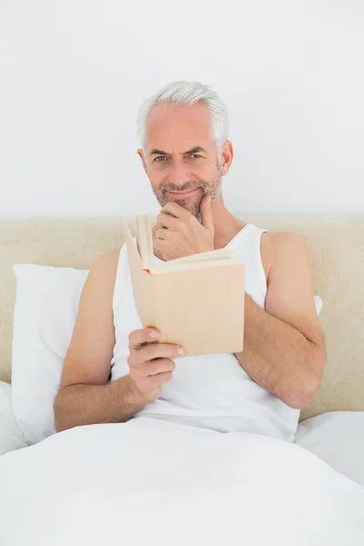 Ontspannen volwassen man lezing boek in bed — Stockfoto