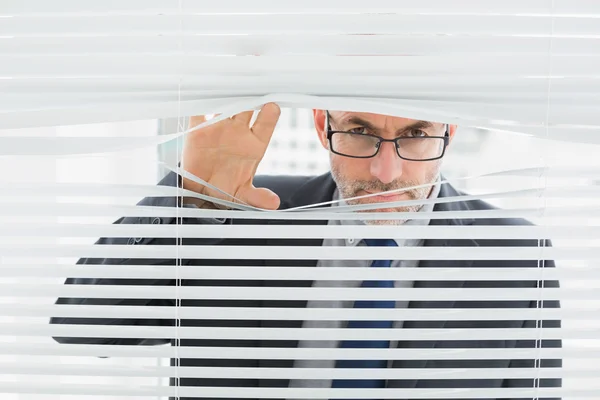 Primer plano de un hombre de negocios mirando a través de las persianas en la oficina — Foto de Stock