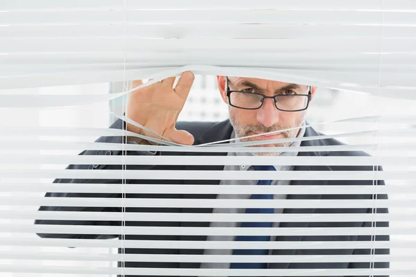 Nahaufnahme eines Geschäftsmannes, der durch Jalousien im Büro blickt — Stockfoto