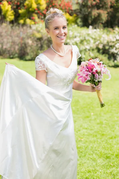 Hübsche blonde Braut mit Blumenstrauß und ihrem Kleid — Stockfoto