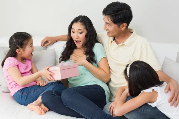 Família apresentando mãe surpresa com uma caixa de presente na sala de estar — Fotografia de Stock