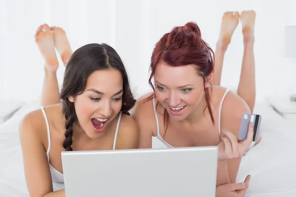 Cheerful female friends doing online shopping in bed — Stock Photo, Image