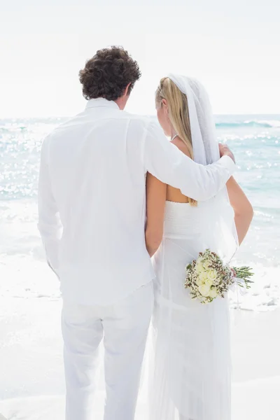 Bride and groom looking out to sea embracing — Stock Photo, Image