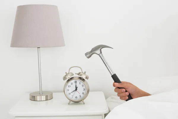 Hand smashing alarm clock with hammer in bed — Stock Photo, Image