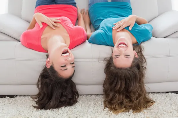 Amigos alegres deitados de cabeça para baixo no sofá em casa — Fotografia de Stock