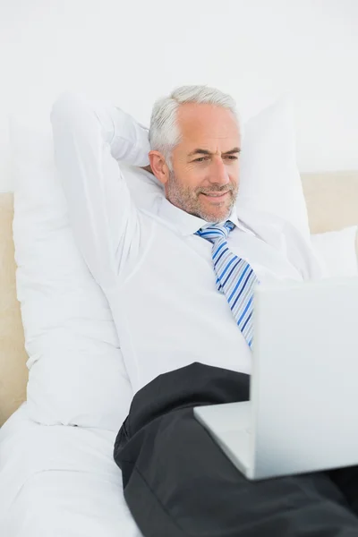 Mature businessman looking at laptop in bed — Stock Photo, Image