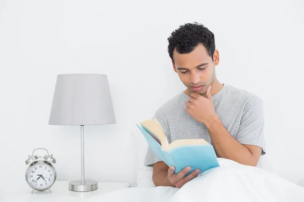 Entspannter junger Mann liest Buch im Bett — Stockfoto