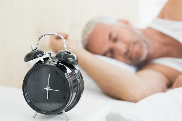 Mann schläft im Bett mit Wecker im Vordergrund — Stockfoto