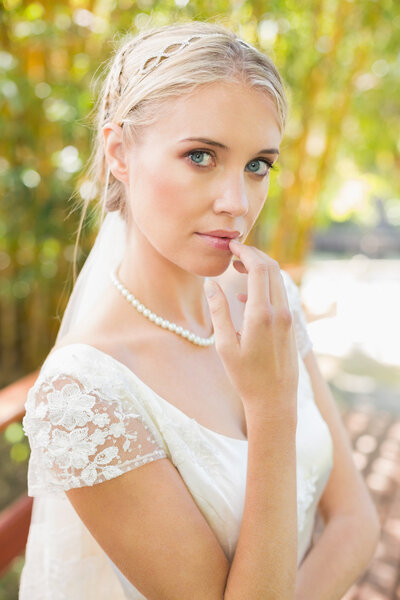 Pretty smiling blonde bride standing on a bridge looking at camera