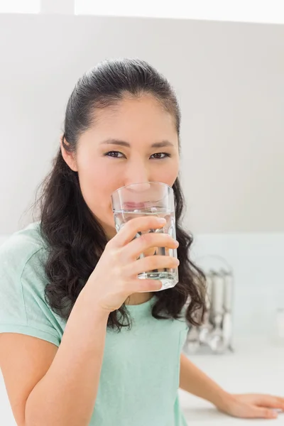 Primo piano di una giovane donna che beve acqua in cucina — Foto Stock