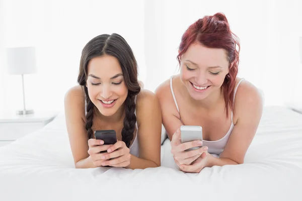 Smiling female friends text messaging on bed — Stock Photo, Image