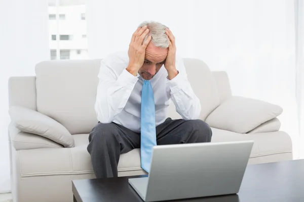 Bezorgde zakenman met hoofd in handen voor laptop thuis — Stockfoto