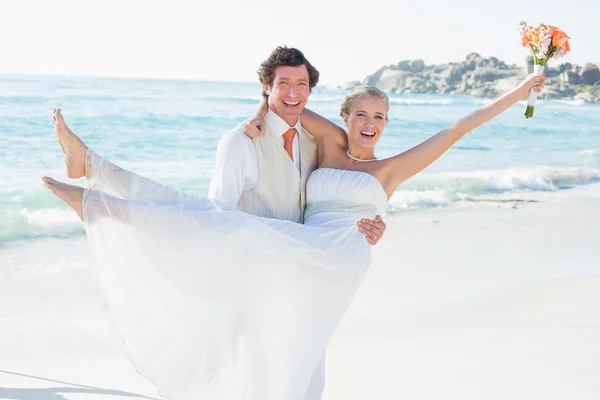 Laughing groom carrying his pretty blonde wife smiling at camera — Stock Photo, Image