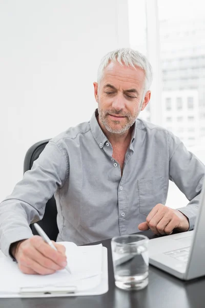 Empresário escrevendo notas ao usar laptop na mesa de escritório — Fotografia de Stock