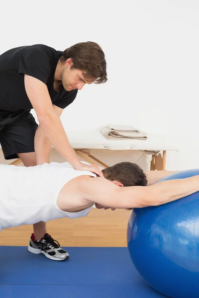 Sjukgymnast hjälpa ung man med yoga boll — Stockfoto