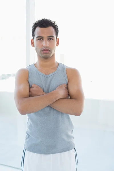 Fit young man standing with arms crossed in fitness studio — Stock Photo, Image