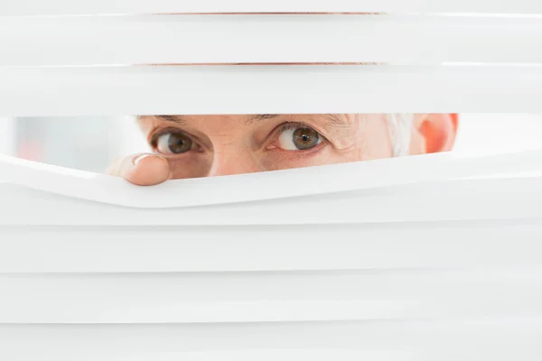 Close-up portrait of a businessman peeking through blinds — Stock Photo, Image