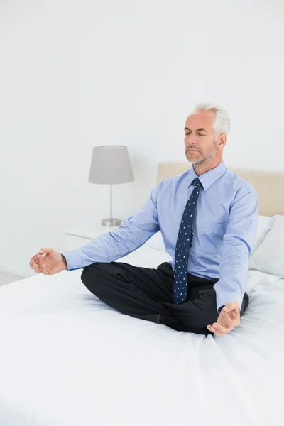 Relaxed mature businessman sitting in lotus posture on bed — Stock Photo, Image