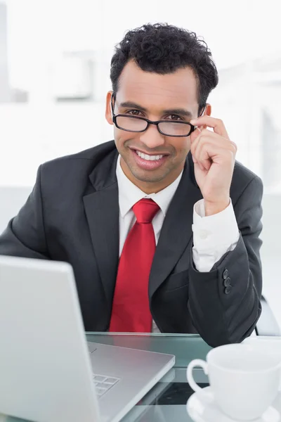 Empresário sorridente com laptop sentado na mesa do escritório — Fotografia de Stock