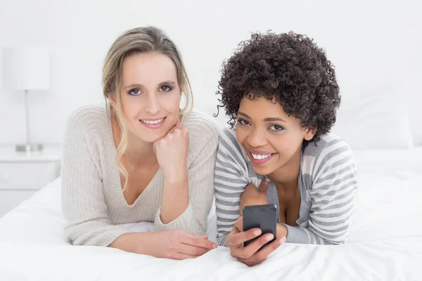 Two smiling female friends reading text message in bed — Stock Photo, Image