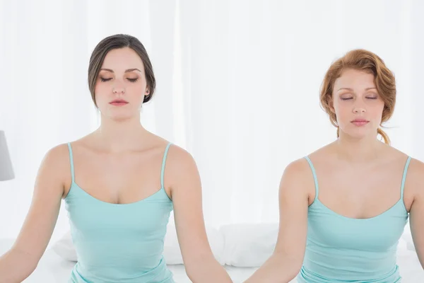 Mujeres con los ojos cerrados sentadas en postura de meditación en la cama — Foto de Stock