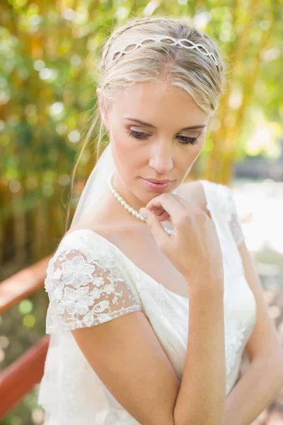 Pretty smiling blonde bride standing on a bridge looking down — Stock Photo, Image