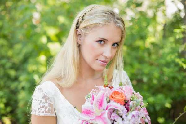 Blonde bride holding big bouquet smiling at camera — Stock Photo, Image