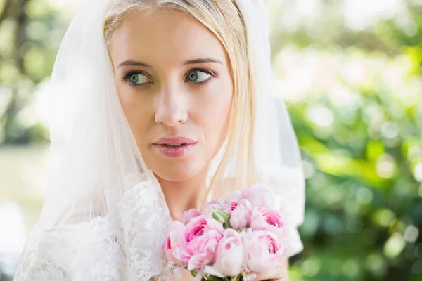 Lächelnde Braut mit Schleier über dem Gesicht hält Strauß in die Kamera — Stockfoto