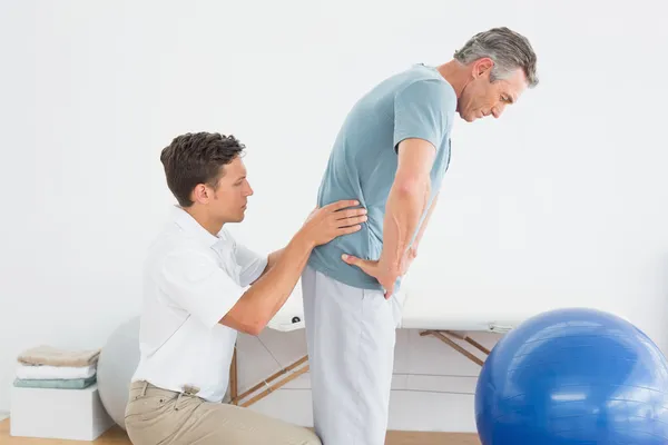 Therapist massaging mans lower back in gym hospital Stock Photo