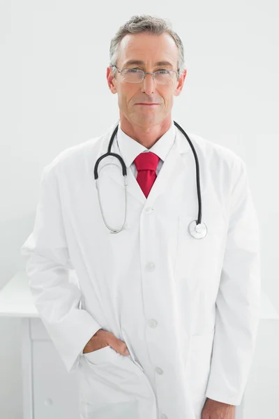 Médico varón sonriente escribiendo un informe en el consultorio Imagen de stock